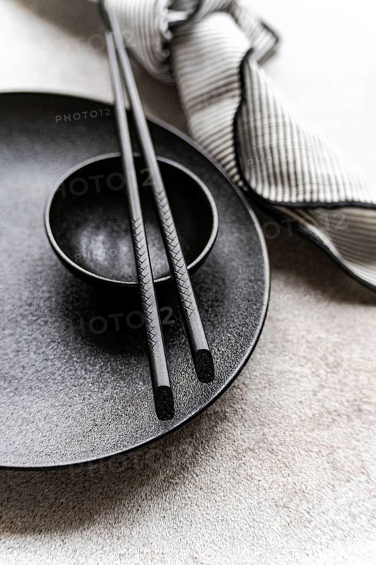 A minimalist black and white table setting featuring chopsticks on a textured plate, complemented by a striped napkin. Perfect for a modern dining theme