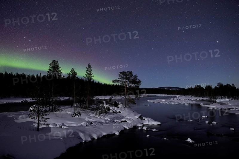 Aurora borealis in green colors over lake in snow covered landscape at night, Lapland, Finland