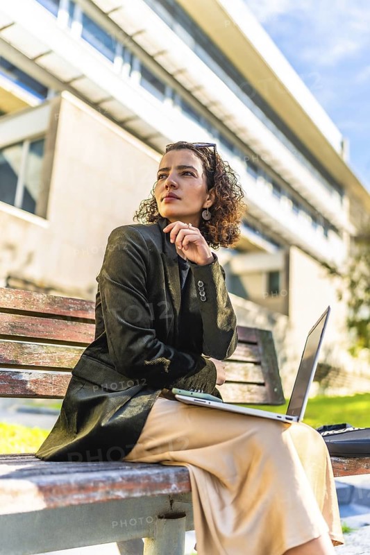 Vertical photo of an arab woman entrepreneur working with laptop outdoors sitting on bench