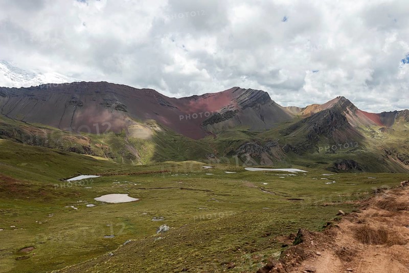 Lush green meadows and sparse glacial lakes set against the dramatic backdrop of the Ausangate mountains in the Andes of Peru, showcasing the region's stunning natural beauty