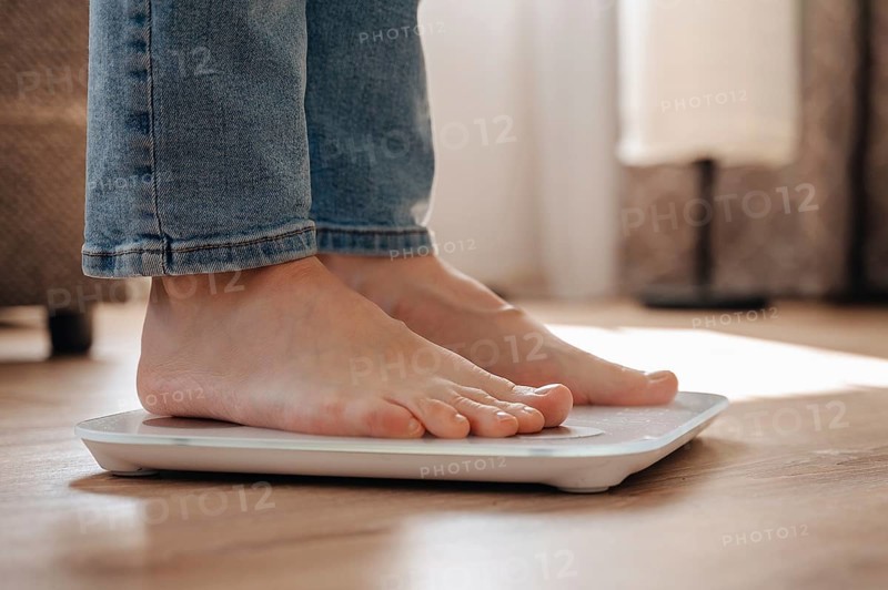 A young woman stands on scales at home, emphasizing a personal weight loss journey. The image captures the concept of health awareness, fitness goals, and lifestyle change