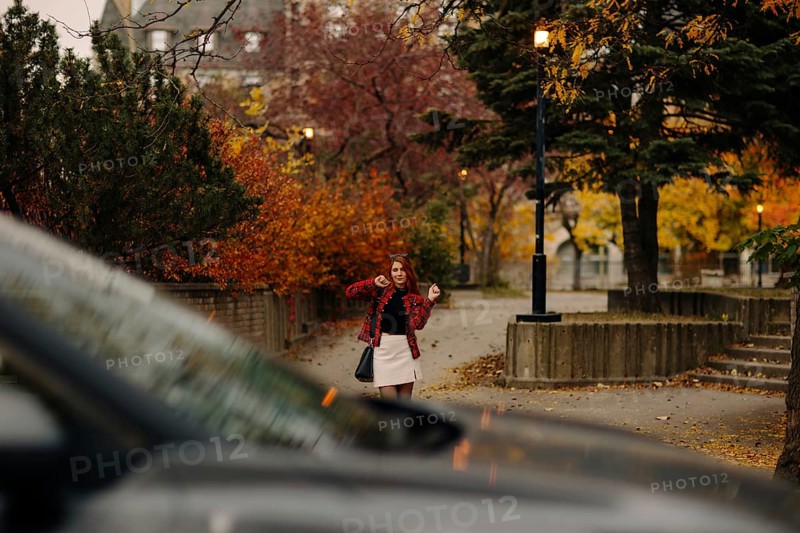 A woman in a red plaid jacket poses joyfully on a Montreal street, surrounded by vibrant autumn foliage and urban scenery, capturing the essence of the fall season