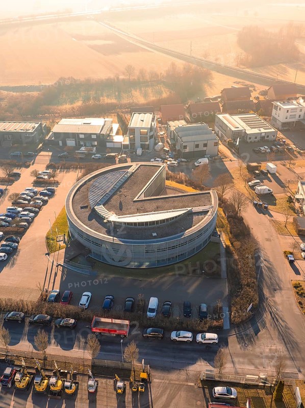 Round industrial building with parked cars and surrounding streets from aerial view in sunny weather, Gültstein, Herrenberg, Germany