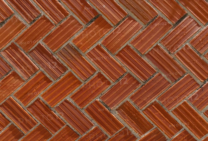 Face brick wall with a classic herringbone pattern. The red-toned bricks are arranged diagonally, creating a dynamic visual effect. Perfect for background, architectural, and construction themes