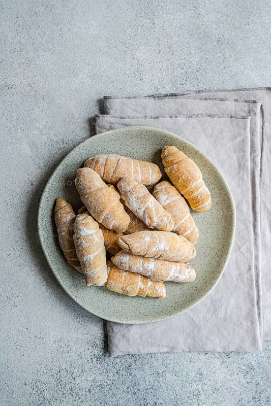 From above, a plate of freshly baked homemade croissants is artfully arranged on a stone-textured surface, showcasing the golden, flaky pastries coated with a dusting of flour