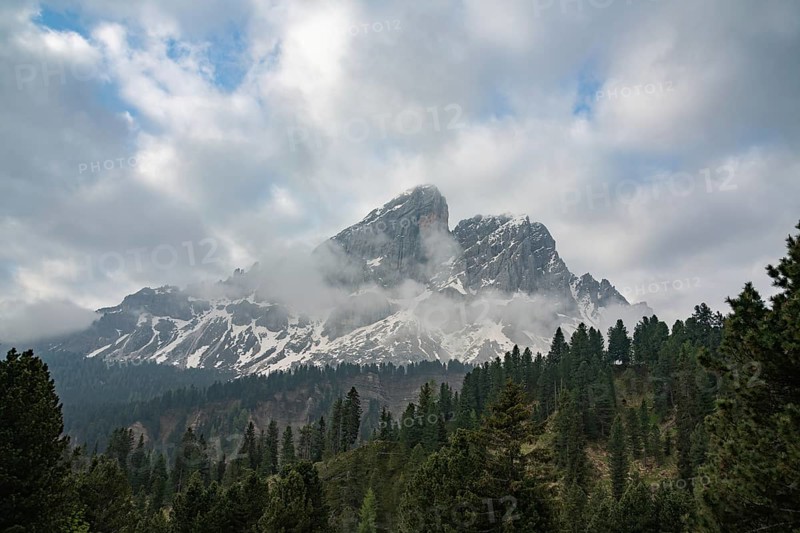 Breathtaking view of the Dolomites mountains in the Cortina d'Ampezzo area, Italy, showcasing snow-capped peaks surrounded by lush green forests under a cloudy sky