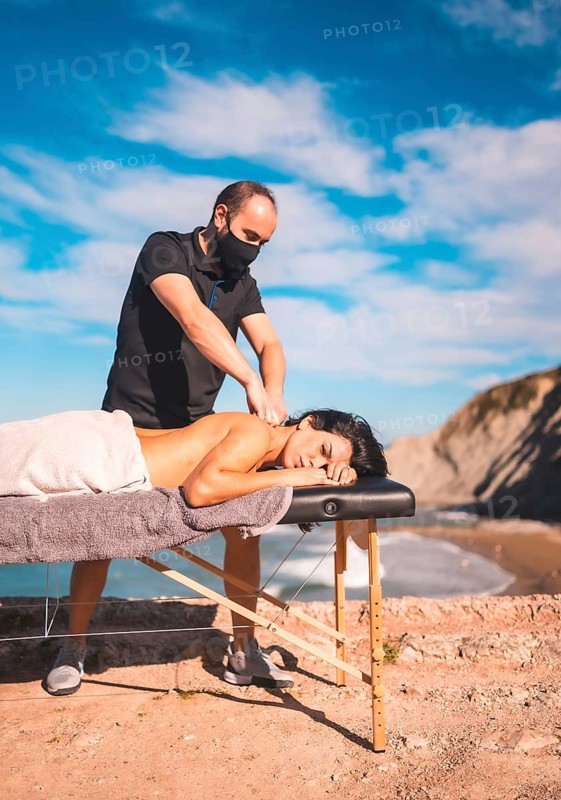 Massages on the coast near the sea, masseuse with face mask in the coronavirus pandemic