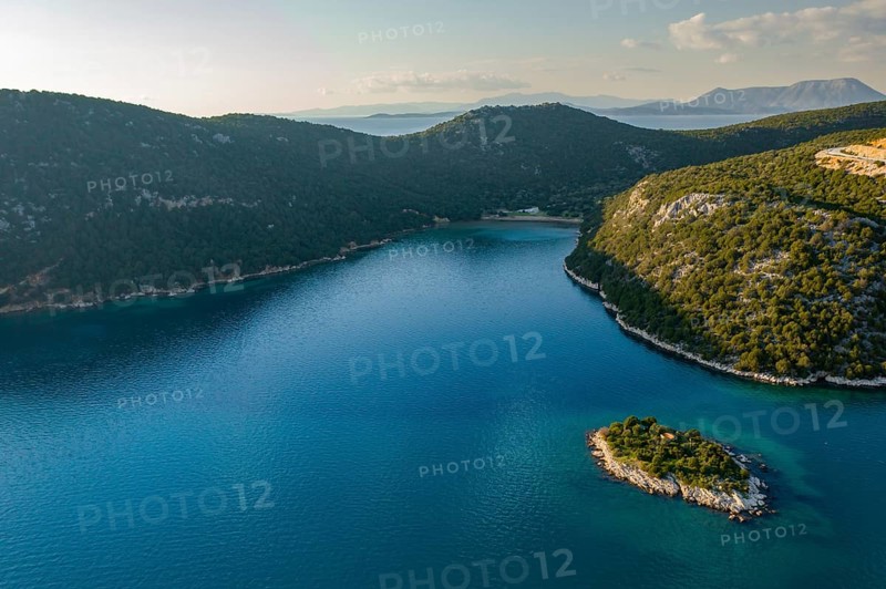 Stunning drone shot of Marathias wild beach, showcasing a peaceful cove with crystal-clear blue waters, lush green hills, and a small island bathed in soft sunlight