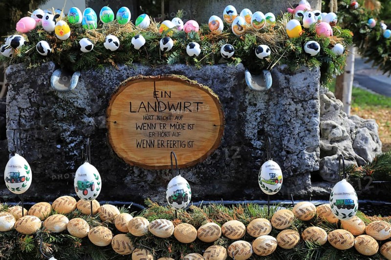 Easter decoration, Franconian Switzerland, Easter fountain, here in the Bamberg district, Upper Franconia, Bavaria, Germany, Easter fountain with decoration on agricultural themes. Easter eggs with stickers from agricultural machinery or decor from tractor tracks. Farmer sign, a decorative arrangement with eggs and a saying about farmers presented on wood
