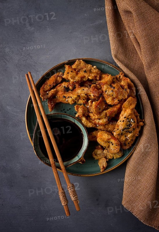 Fried meat in batter, deep-fried, with sesame seeds, and soy sauce, on a gray table, there are no people