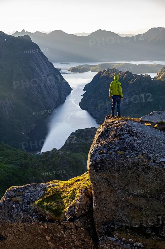 Mountaineer, young man standing on rocks and looking into the distance, at sunrise, fjord Trollfjord and mountains, hike to Trollfjord Hytta, at Trollfjord and Raftsund, Lofoten, Nordland, Norway