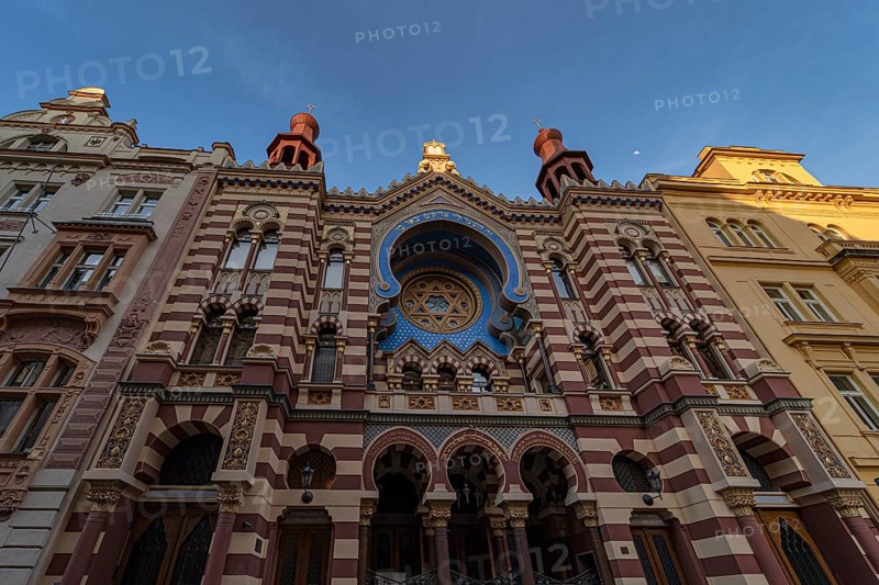 Majestic facade of a historic synagogue in Prague, showcasing Moorish Revival architecture. The ornate details and vibrant colors are highlighted against a clear evening sky
