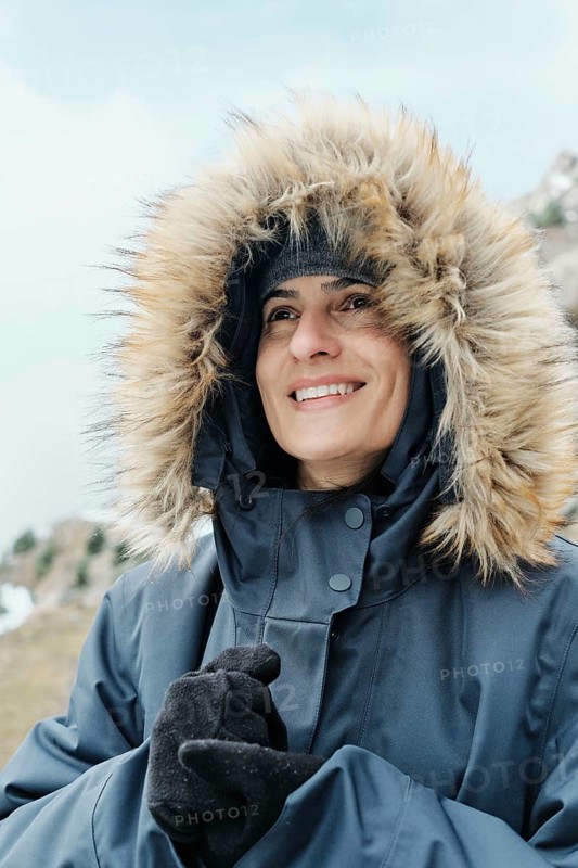 A cheerful woman wearing a thick winter coat with a fur-lined hood, smiling while enjoying the cold weather in the Pyrenees