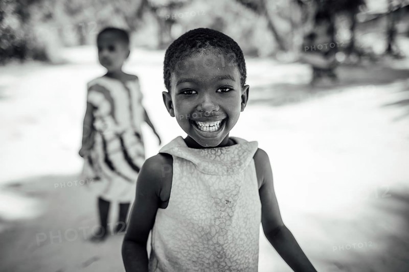 MICHAMVI KAE, ZANZIBAR - OCTOBER 17, 2025: A joyful young girl with a radiant smile looks directly at the camera in a black and white portrait, featuring a blurred background in Zanzibar