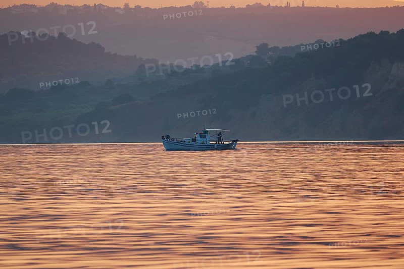 Fishing boat on pastel-colored water in front of a hilly landscape at sunrise, Navarino Bay, Pylos, Peloponnese, Greece
