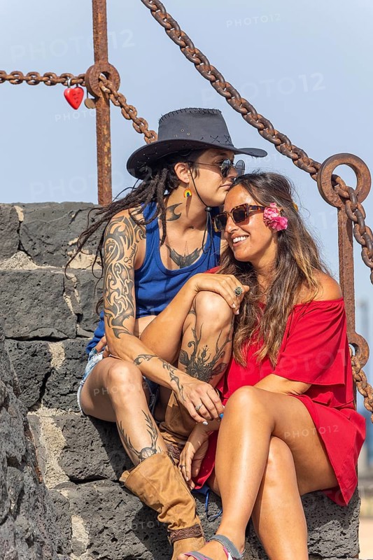 A joyful lesbian couple shares a tender moment on stone steps during summer. Embracing under a sunny sky, their happiness shines, celebrating love and pride