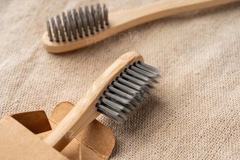 From above view of bamboo toothbrushes with soft bristles on a textured beige fabric. Packaged eco-friendly, sustainable design emphasizes zero waste and reusable materials