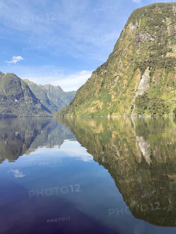 Mountains with reflections in the water against a blue sky in Doubtful Sound, South Island, New Zealand, Oceania