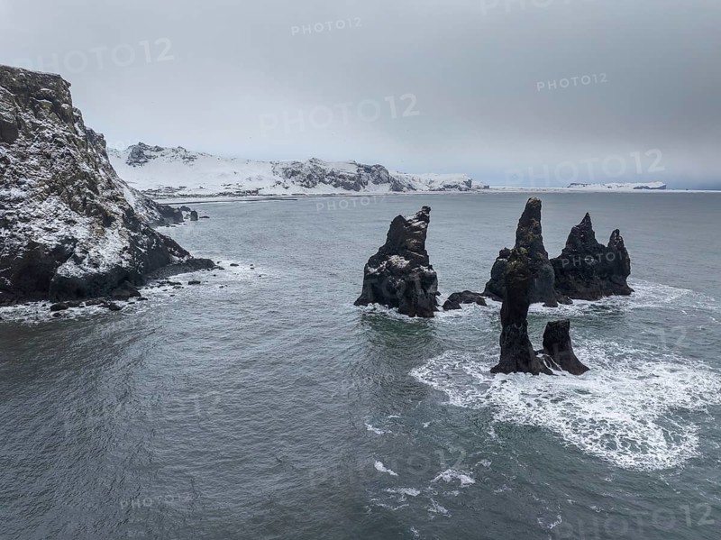 Stunning sea stacks rise from the ocean along Vik's snowy coastline in Iceland. Capturing nature's raw beauty with snow-dusted rocks and icy waters under a moody sky