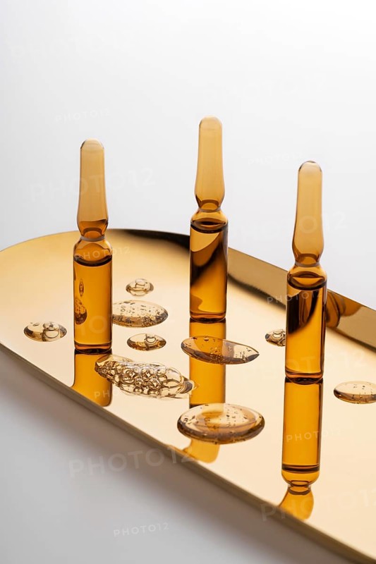 Aesthetic arrangement of cosmetic ampoules filled with anti-aging serum, placed on a reflective golden surface, highlighting their luxurious nature and the promise of youthful skin