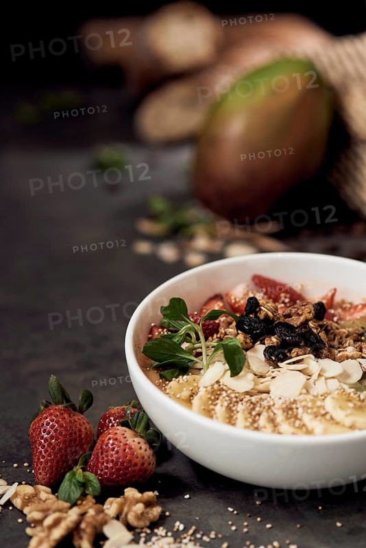 A nutrient rich breakfast natural bowl filled with strawberries, banana slices, nuts, raisins, and leafy greens. Set on a dark surface, highlighting fresh ingredients