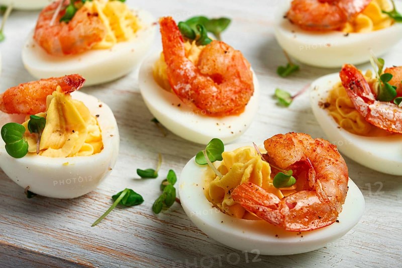 Boiled eggs stuffed with yolk and seasoned with mayonnaise, stuffed eggs with shrimp, on a white wooden chopping board, selective focus, close-up, without people