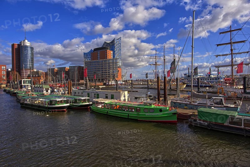 View of boats and ships in harbor surrounded by city skyline under a partly cloudy blue sky, Hamburg, Germany