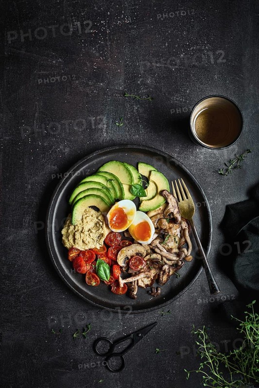 Overhead full plate of delicious dish with hummus from fried champignons and boiled eggs with tomatoes and avocado served fresh leaves of basil