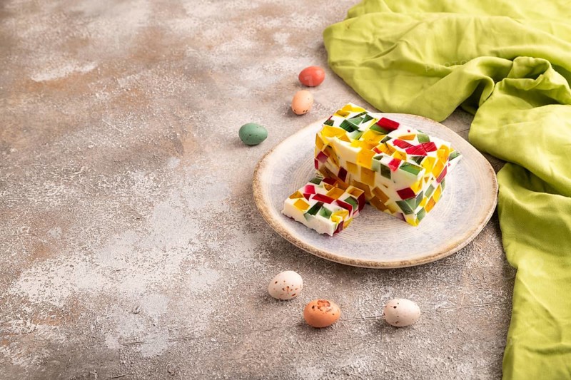 Colored Fruit and milk jelly on brown concrete background and green linen textile, side view, copy space, minimalism