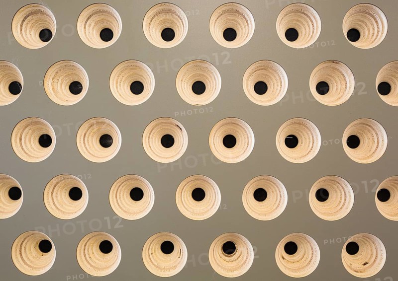 An intricate geometric pattern of evenly spaced round wooden structures with black centers on a gray background, creating a contemporary and artistic ambiance in club wall