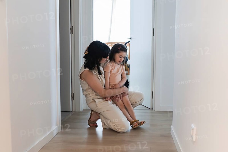 A young family scene with a loving mother and her daughter sharing a tender moment in a bright hallway, conveying warmth and connection in a serene home atmosphere