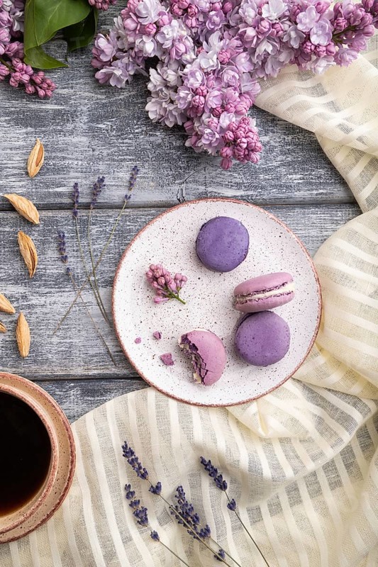 Purple macarons or macaroons cakes with cup of coffee on a gray wooden background and white linen textile. Top view, flat lay, close up