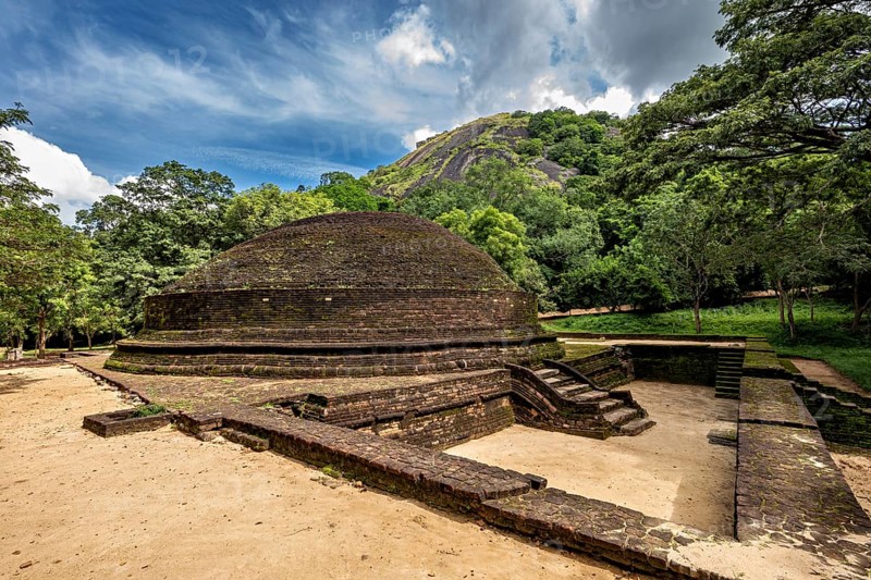 Round stupa on an open area with blue sky and green surroundings, temple ruins near Sigiriya in Sri Lanka