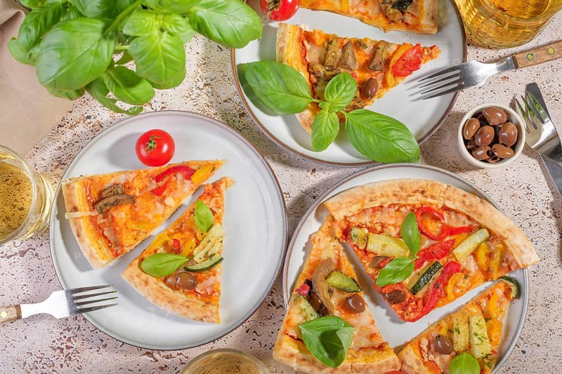 A rustic scene featuring vegetarian pizza slices topped with fresh basil, zucchini, eggplant, and cheese. Set on a light background, this inviting meal offers a taste of Mediterranean cuisine