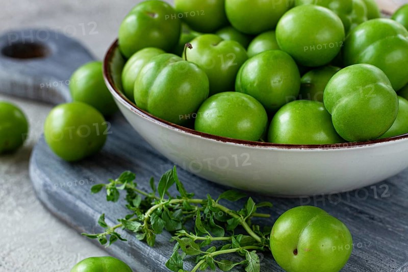 Tkemali, green cherry plum, in a bowl, on a gray table, top view, natural light, no people