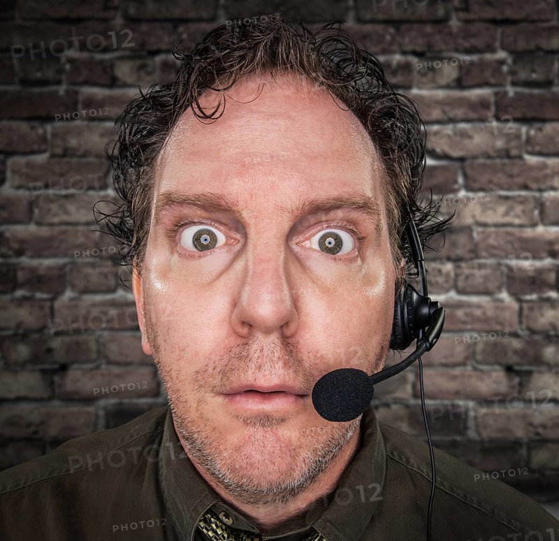Stunned Businessman Wearing Phone Headset In Office With Brick Wall Background