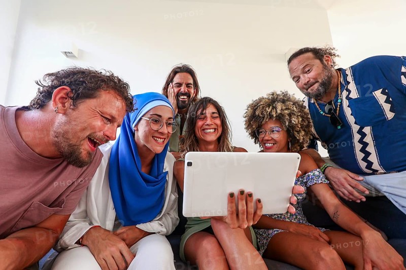 A joyful multiethnic group of friends from different backgrounds gathered around a tablet, sharing laughter and happiness Perfect for themes of friendship, technology, and diversity