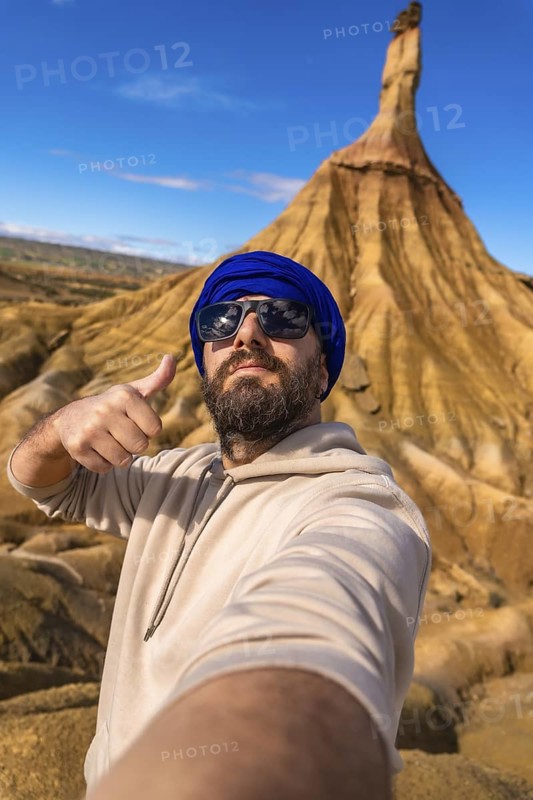 Tourist with blue turban and sunglasses taking a selfie and making thumbs up sign in the bardenas reales desert, navarre, spain