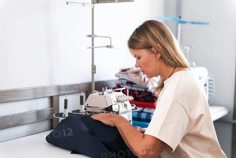 A dedicated woman skillfully operates a sewing machine in a bright and organized workshop, surrounded by materials and tools, illustrating the art of garment creation
