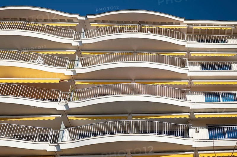 A view of modern apartment balconies featuring a distinct curved design. The light-colored metal railings and geometric shapes create a sleek and contemporary look