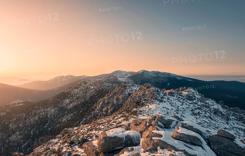 A breathtaking view of Siete Picos in Guadarrama Mountains, Madrid, covered in snow under a golden sunset. The rugged peaks and serene atmosphere captivate the senses