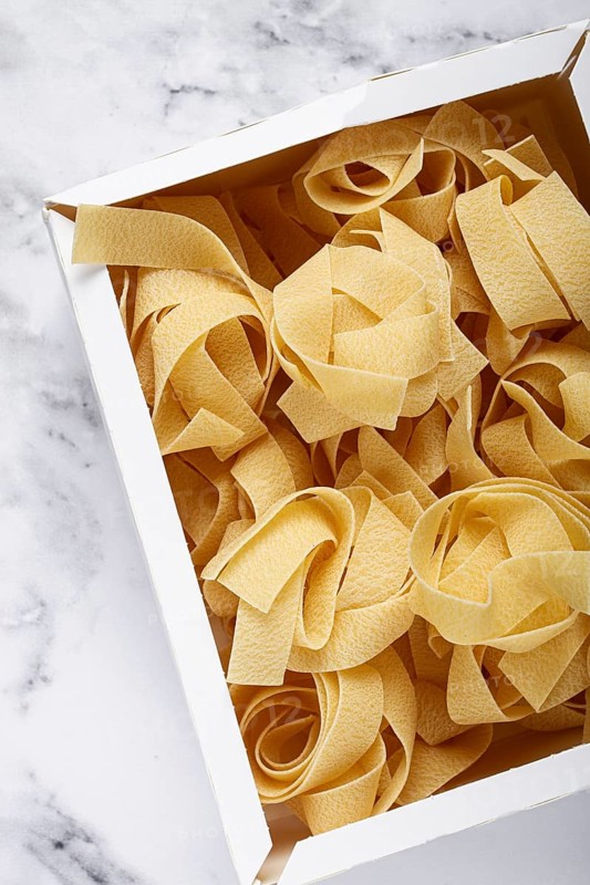 Raw pappardelle pasta, pasta nests, in a paper box, top view, no people