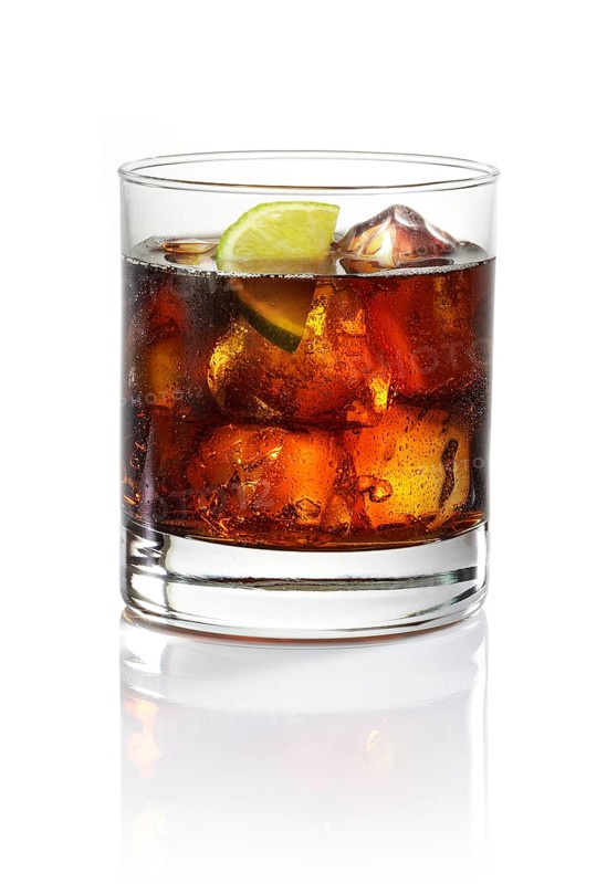 Whisky and cola on ice cube cubes in a tumbler against a white background, half a slice of lime as garnish, studio shot