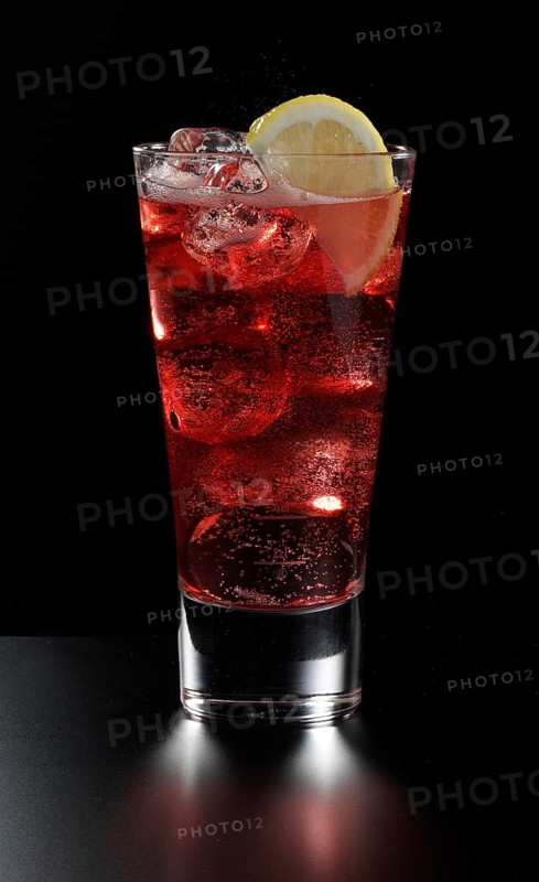 Cocktail Campari Soda in a long drink glass in front of a black background, half a slice of lemon as garnish, studio shot