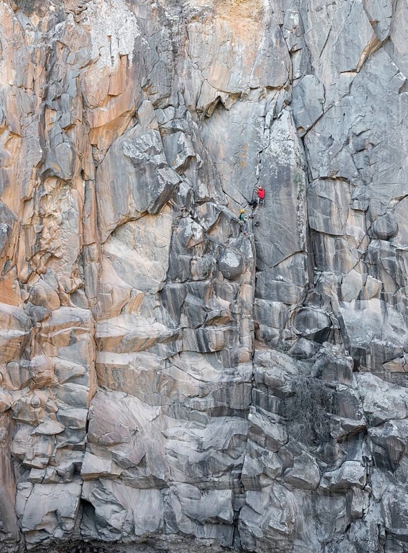 Climbers engage in traditional climbing on a rugged rock face, showcasing endurance and skill. The towering cliffs and natural environment create a thrilling outdoor adventure