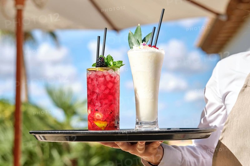 Two vibrant cocktails on a tray, featuring a red berry drink and a creamy pina colada. Captured outdoors on a sunny day, embodying tropical vibes and refreshing flavors