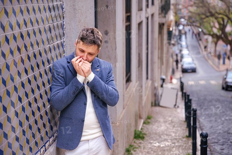 Man musician in a blue blazer and white sweater playing blues on a harmonica with eyes closed, standing outdoors in city street