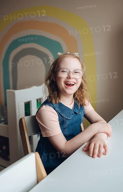 A cheerful girl with Down syndrome enjoys playing in a colorful room. Her joyful expression and the vibrant background create an atmosphere full of happiness and warmth