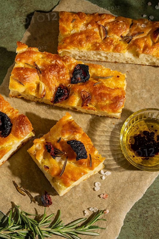 Slices of homemade focaccia topped with rosemary, roasted garlic, and sun dried tomatoes. Served on brown paper with a side of olive oil and balsamic vinegar dip