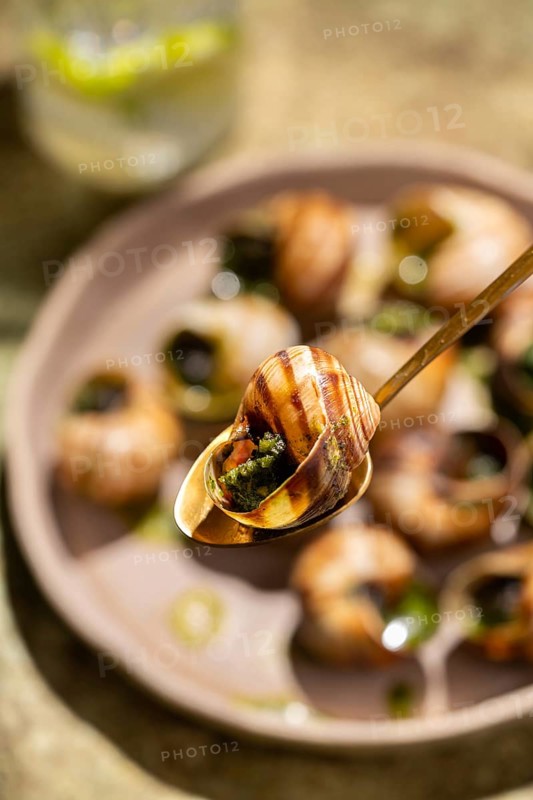 Close-up image of baked escargot garnished with parsley and butter, served in a circular dish with a fork